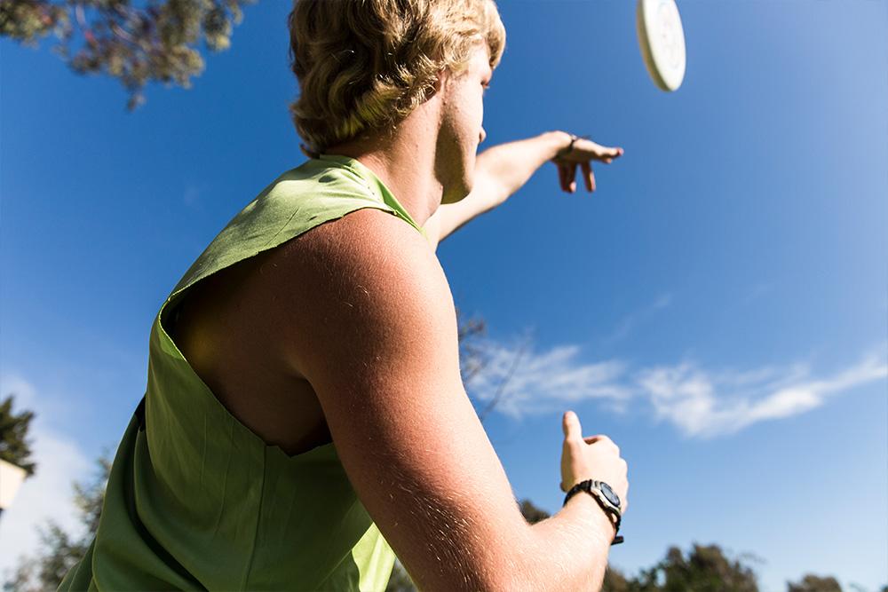 A student makes an overhand toss to his teammate in a game of ultimate frisbee.